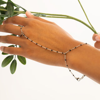 Hand wearing a delicate silver hand chain  with green leaves in the background