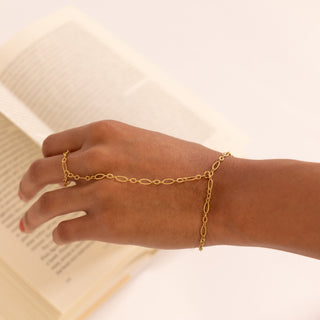 Gold hand chain on a wrist with a blurred book in the background