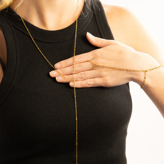 Person wearing a gold necklace and hand chain on a plain background