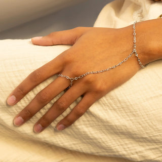 Hand wearing a silver hand chain on a neutral background