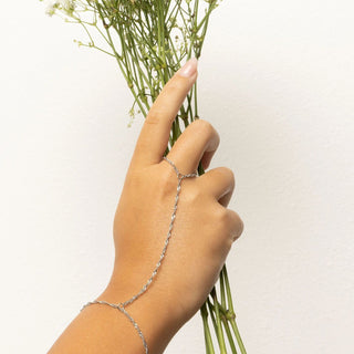 Hand holding a bundle of green stems with a silver Singapore Hand Chain on a light background