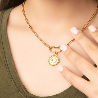 Gold necklace with a pendant worn by a person, close-up of the necklace and hand.