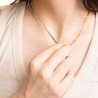 Gold necklace being worn with a hand adjusting it, on a neutral background
