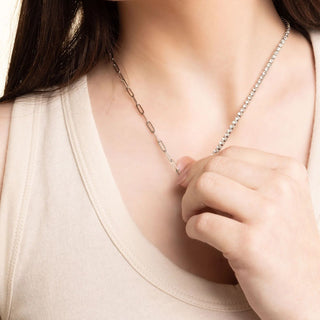 Person wearing a delicate silver necklace with a soft beige background