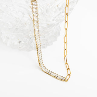 Gold chain necklace with clear stones on a textured white surface