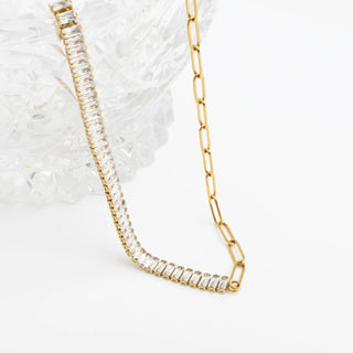 Gold chain necklace with clear gemstones on a textured white surface