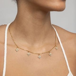 Gold necklace with floral pendants on a person wearing a white top against a neutral background