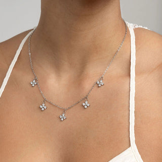 Silver necklace with flower pendants on a person wearing a white top against a neutral background