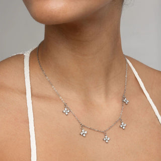 Silver necklace with floral pendants on a person wearing a white top against a neutral background