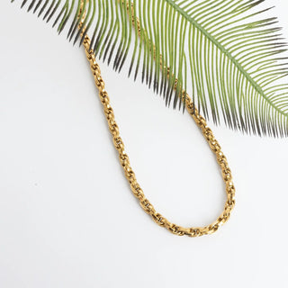Gold chain necklace on a white background with a palm leaf