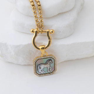 Gold necklace with a horse pendant on a white marble surface