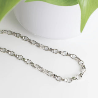Silver chain necklace on a white surface with green leaves in the background