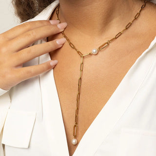 Gold y-shaped chain necklace with pearls worn by a person, against a neutral background