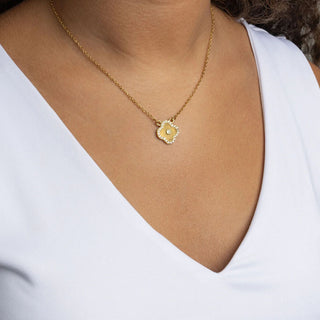 Gold necklace with a floral pendant worn by a person in a white top.