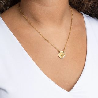 Gold necklace with a floral motif pendant on a person wearing a white shirt