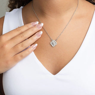 Silver necklace with a floral pendant worn by a person in a white top.