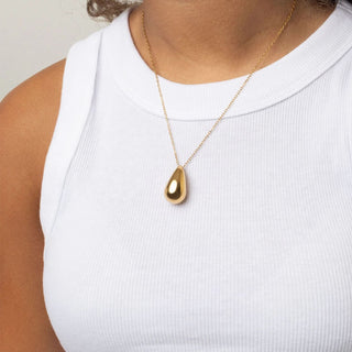 Gold teardrop necklace on a person wearing a white top