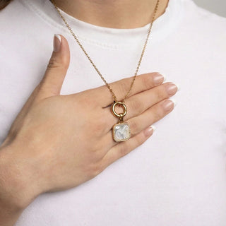 Gold charm holder necklace with a pendant held by a hand against a white background