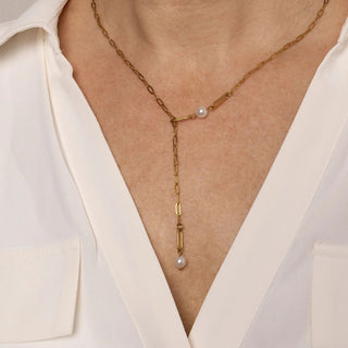 Gold y-shaped necklace with pearl drops worn by a person in a white blouse.