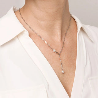 Silver y-shaped necklace with pearls worn by a person in a white shirt