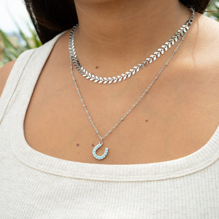 Close-up of a person wearing two silver necklaces with a white top.