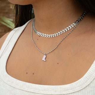 Close-up of a person wearing multiple silver necklaces with a white top.