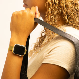 Person wearing a gold smartwatch and holding a black strap.