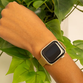 Gold smartwatch on a wrist with green leaves in the background