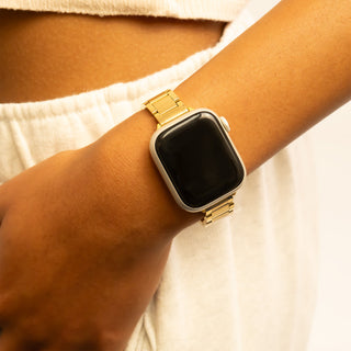 Smartwatch with a gold band on a wrist against a neutral background