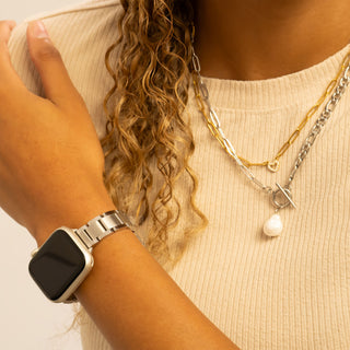 Person wearing a smartwatch and multiple necklaces with a neutral background