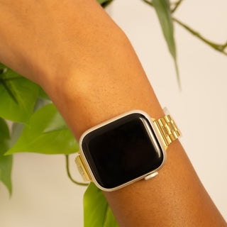 Gold smartwatch on a wrist with a blurred green plant background