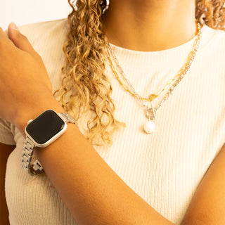 Person wearing a smartwatch and gold necklace with a blurred background