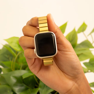 Hand holding a smartwatch with a gold band against a green leafy background