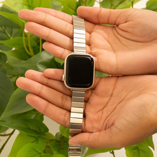 Smartwatch with metal band held in a hand against a green leafy background