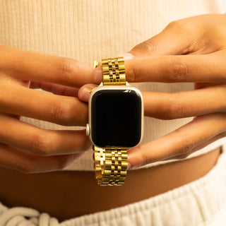 Gold watch with a black screen held between fingers against a neutral background