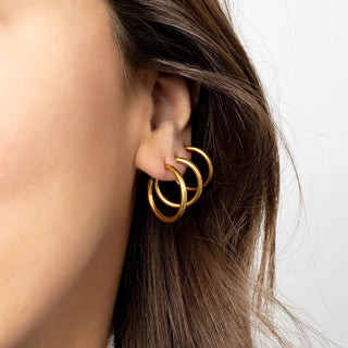 Close-up of a person wearing a gold hoop earring with a neutral background