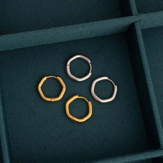 Three hoop earrings in gold and silver on a dark green fabric surface