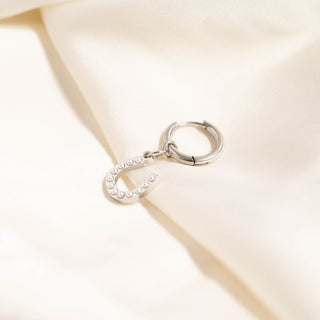 Silver hoop earring with a small round charm on a beige fabric background