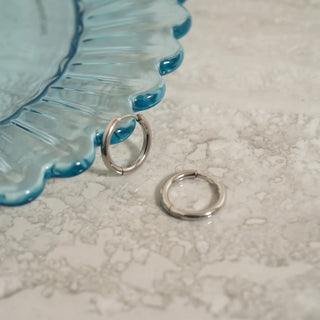 Two silver hoop earrings on a textured surface with a blue decorative object in the background.