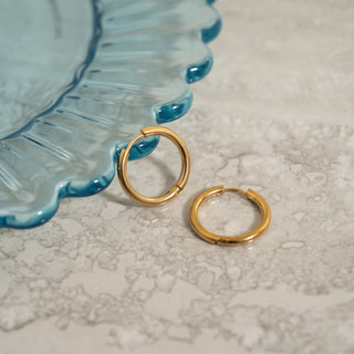 Gold hoop earrings on a textured surface with a blue decorative plate in the background