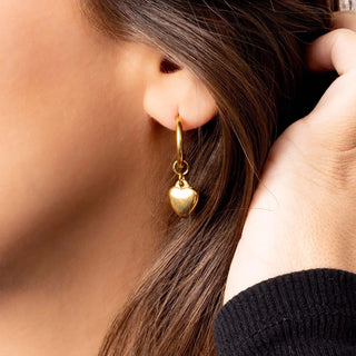 Gold heart-shaped earring worn by a person with brown hair.