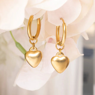 Gold heart-shaped earrings on a soft floral background