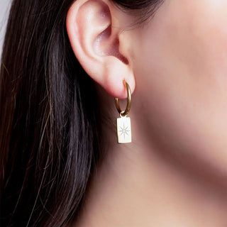 Gold hoop earring with a star-shaped tag worn by a person