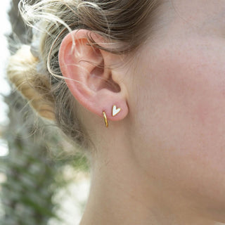 Close-up of an ear wearing a gold heart-shaped earring with a blurred natural background
