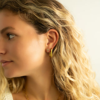 Close-up of a woman wearing gold hoop earrings with Cross stud earrings with a blurred background