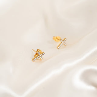 Gold cross earrings with small cubic zirconias on a beige satin background