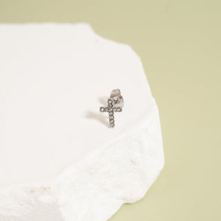 Silver cross earring on a white cloth with a beige background