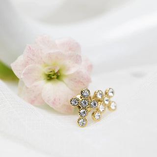 Gold earrings with clear stones on a white background with a pink flower.