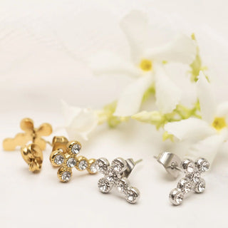Gold and silver cross-shaped earrings on a white background with flowers.