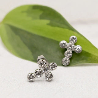 Silver cross-shaped earrings with clear stones on a green leaf